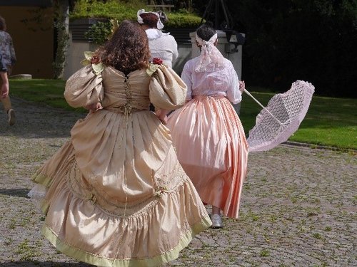 Drei Kinder, verkleidet in prunkvollen Ballkleidern, laufen über den Innenhof des Schlossplatzes. 