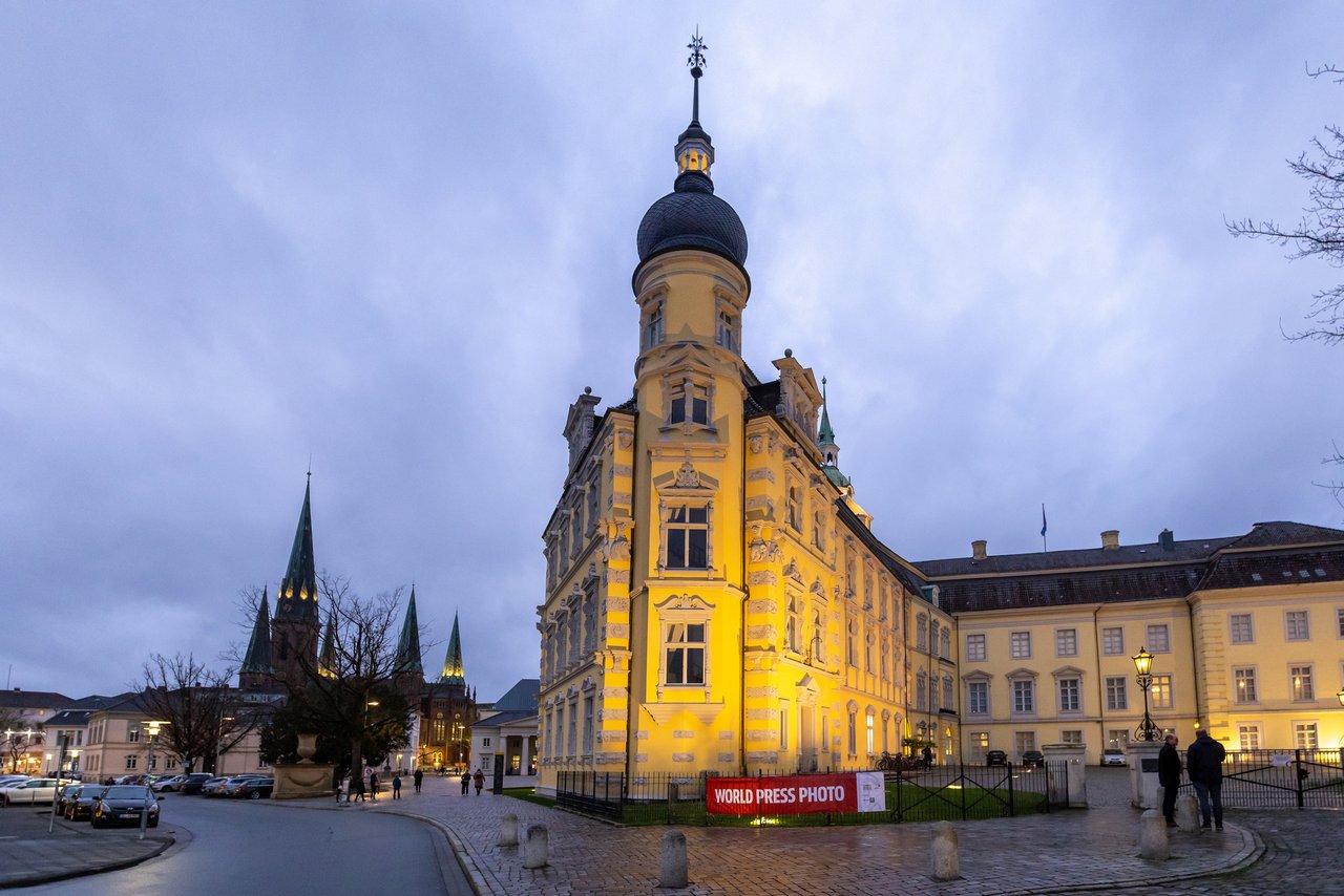 Das Oldenburger Schloss in der Dämmerung, am Zaun hängt ein Banner der Ausstellung „World Press Photo 2023”