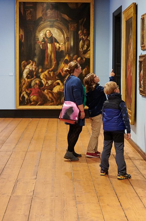 Eine Frau und zwei Kinder betrachten ein großes Gemälde.